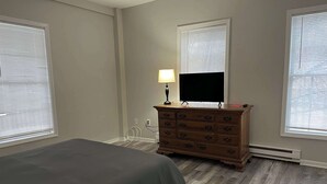 Un dormitorio con cama, cómoda, televisor y ventanas.