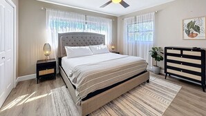 Ein Schlafzimmer mit einem Bett, einem Deckenventilator, einem Nachttisch, einer Wandkabine und einer Pflanze.