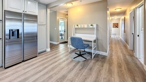 Eine moderne Küche mit einem Edelstahlkühlschrank, einer weißen Arbeitsplatte und einem blauen Stuhl in einem Flur mit Holzdielen und weißen Wänden.