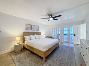 A bedroom with a wooden bed, a ceiling fan, and a view of the outside through large doors. - 20002 Gulf Blvd, Penthouse 5 (Indian Shores)