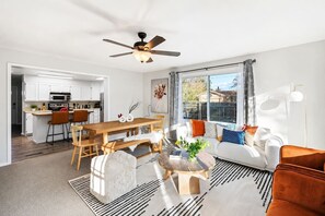 A modern living room with a dining area, a ceiling fan, and a large window with a view. - Modern Stay Home w Game Rooms | Olde Town Arvada (Arvada)