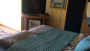 Une chambre d’hôtel avec un lit, un téléviseur posé sur un meuble, un bureau et un tableau accroché au mur.