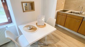 A modern kitchen with a white countertop, a sink, and wooden cabinets. There is a dining table with two chairs and a menu on the table. - Charming studio in center (Cluj-Napoca)