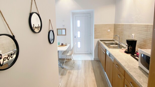 A modern kitchen with wooden cabinets, a countertop with a coffee maker, and a dining area with a chair and table. - Charming studio in center (Cluj-Napoca)