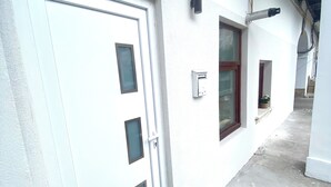 A white exterior wall with a door, a window, and a wall-mounted electrical box. - Charming studio in center (Cluj-Napoca)