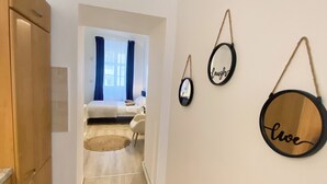 A modern apartment with a wooden wardrobe, a hallway leading to a bedroom with a bed and a chair, and three wall-mounted mirrors with words. - Charming studio in center (Cluj-Napoca)