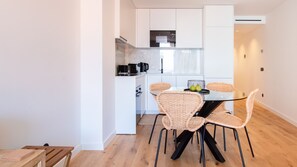Une cuisine moderne avec des meubles blancs, un plan de travail noir et un coin repas comprenant des chaises en osier et une table en verre.