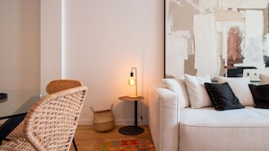 Un salón moderno con un sofá blanco, un sillón de mimbre, una lámpara de pie y un cuadro abstracto grande en la pared.
