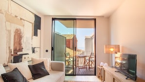 Una sala de estar moderna con un sofá, un televisor y un balcón con una mesa y sillas.