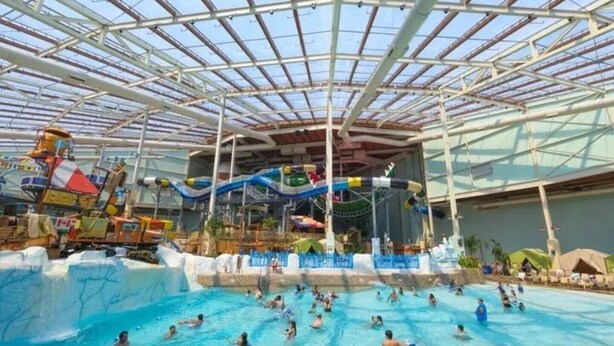Um parque aquático interno com uma piscina grande, toboáguas e área coberta.
