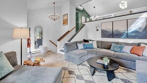Una sala de estar moderna con un sofá modular gris, una mesa de centro y una escalera que conduce a un piso superior.