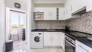 Eine moderne Küche mit weißen Schränken, einer Waschmaschine, einem Backofen und einer Mikrowelle.