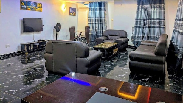 Un salon moderne avec des canapés en cuir noir, un téléviseur à écran plat et un sol en marbre.