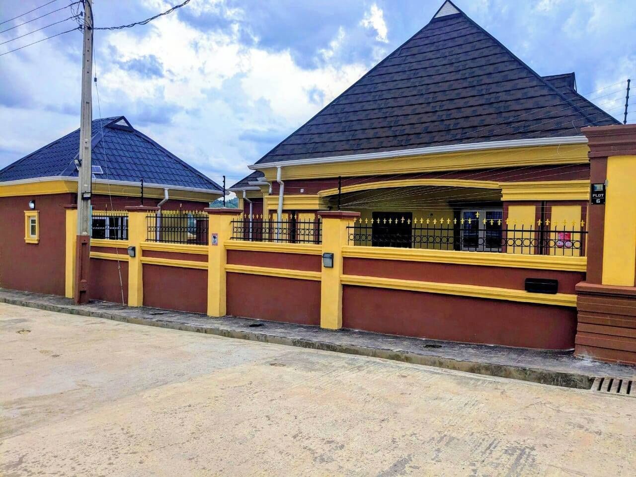 A building with a dark roof and yellow walls, featuring a gated entrance and a visible sign.