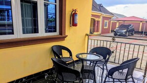 Un espace extérieur abrité, doté d’un extincteur fixé au mur, d’une table en verre et de quatre chaises en osier.