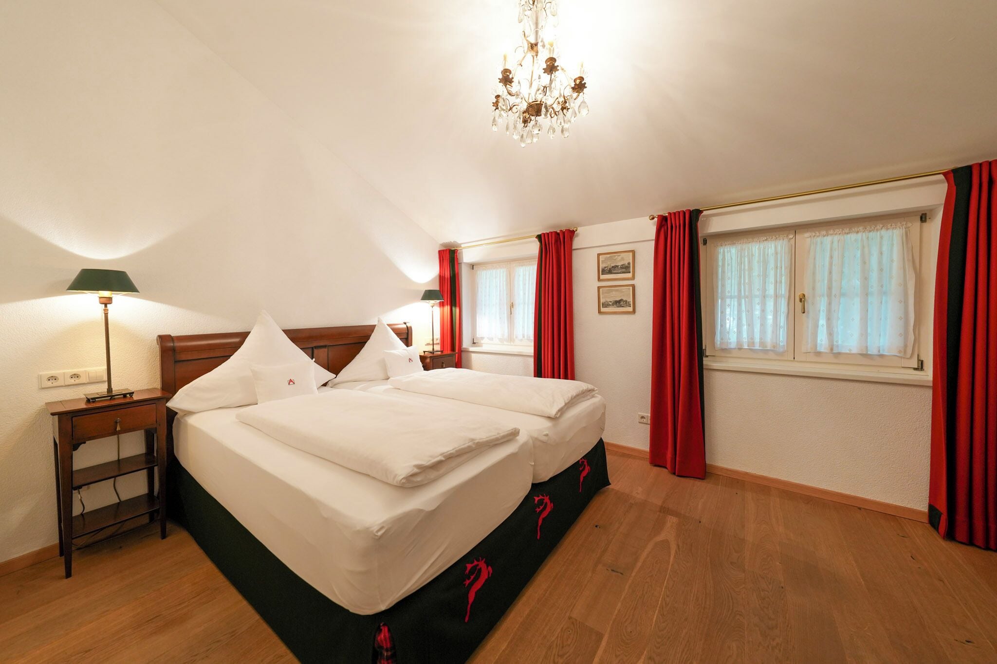 Una camera d'albergo con un letto matrimoniale, un comodino, una lampada, un lampadario e tende rosse.