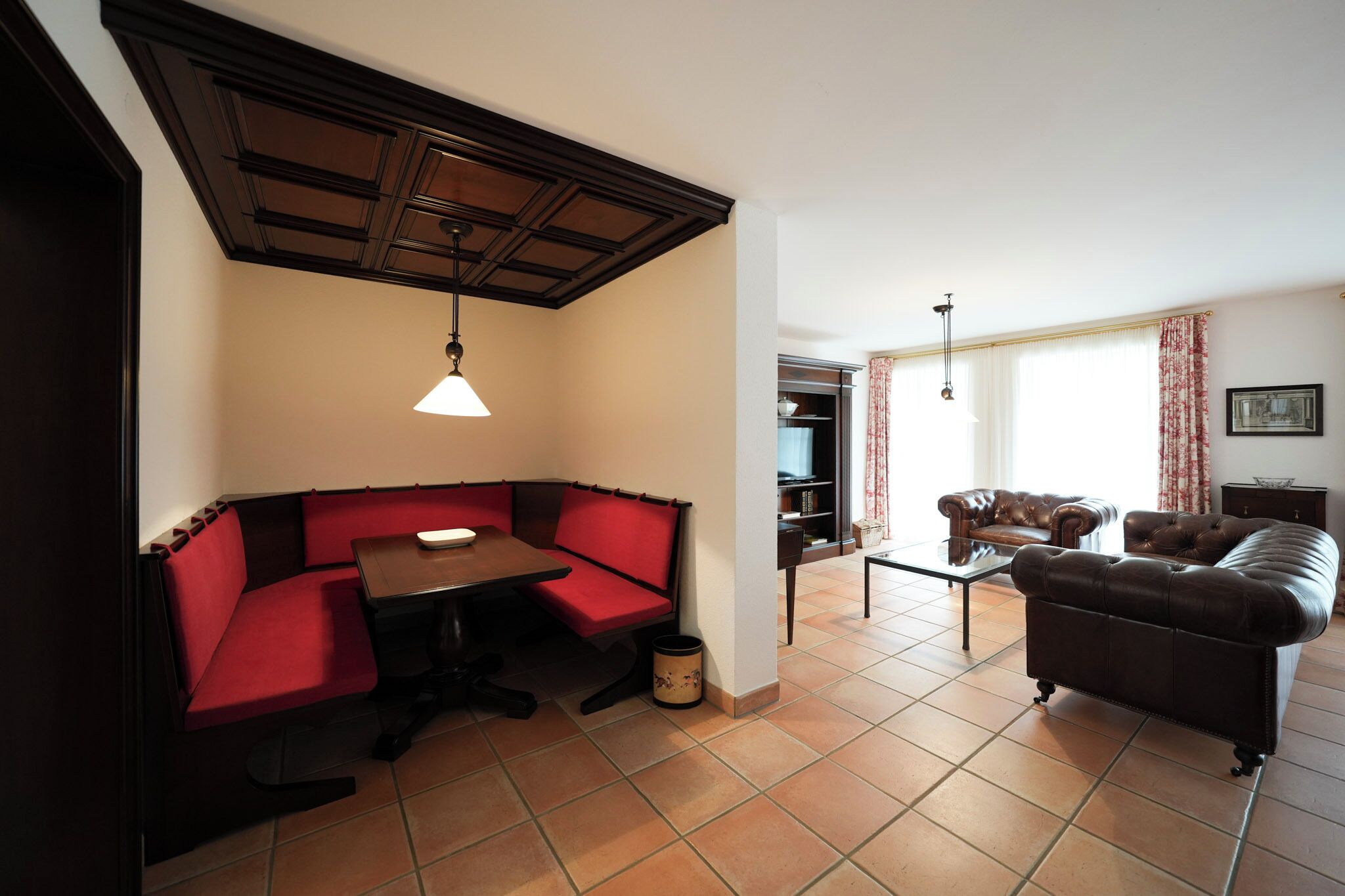 A living room with a red sofa, a brown leather couch, a dining table, and a ceiling with a wooden panel design.