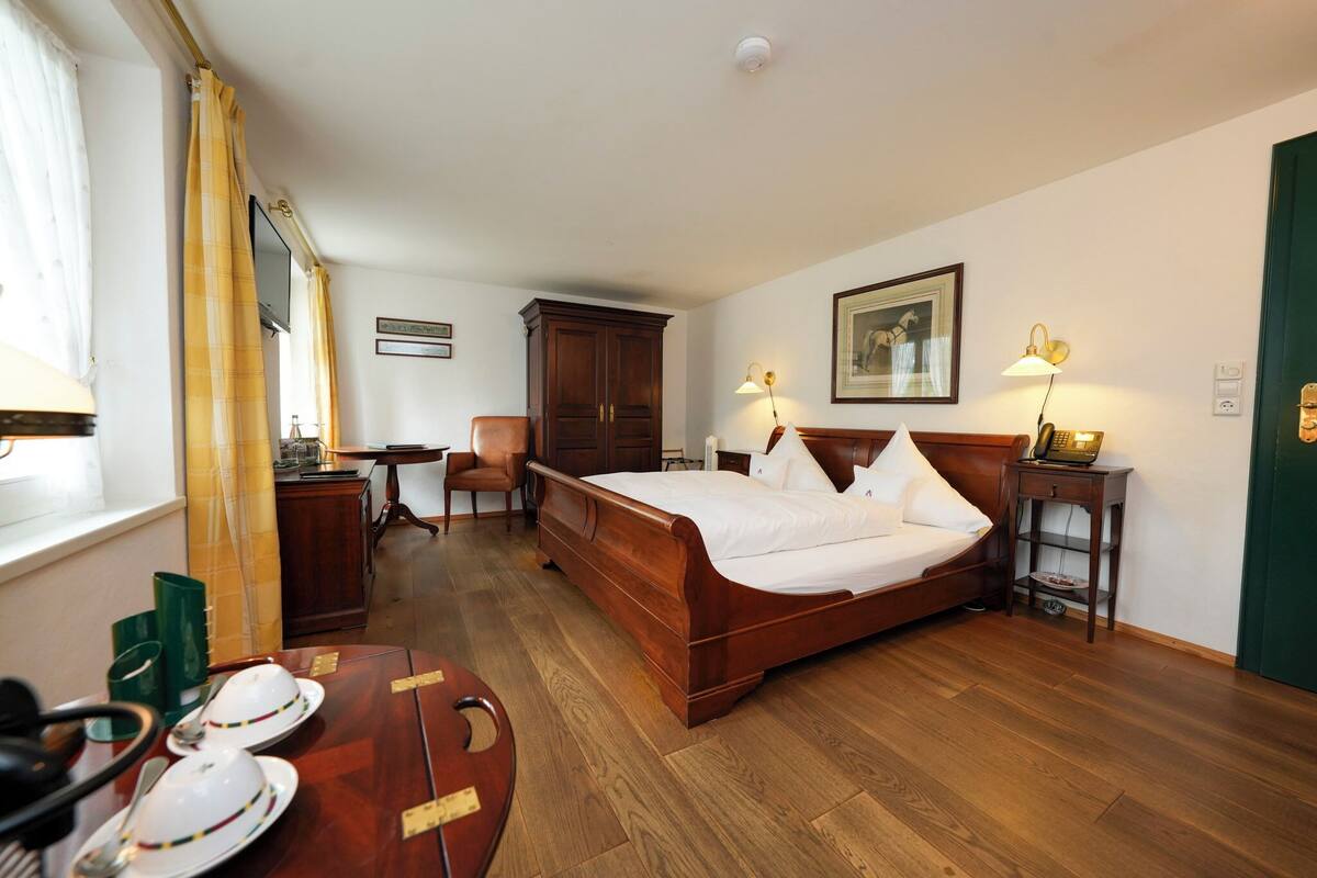 Habitación de hotel con una cama de madera, un escritorio, una silla y una mesa de comedor dispuesta con platos y cubiertos.