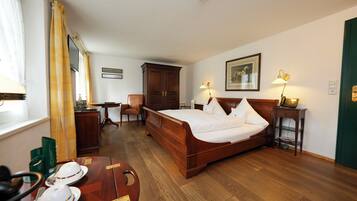 Habitación de hotel con una cama de madera, un escritorio, una silla y una mesa de comedor dispuesta con platos y cubiertos.
