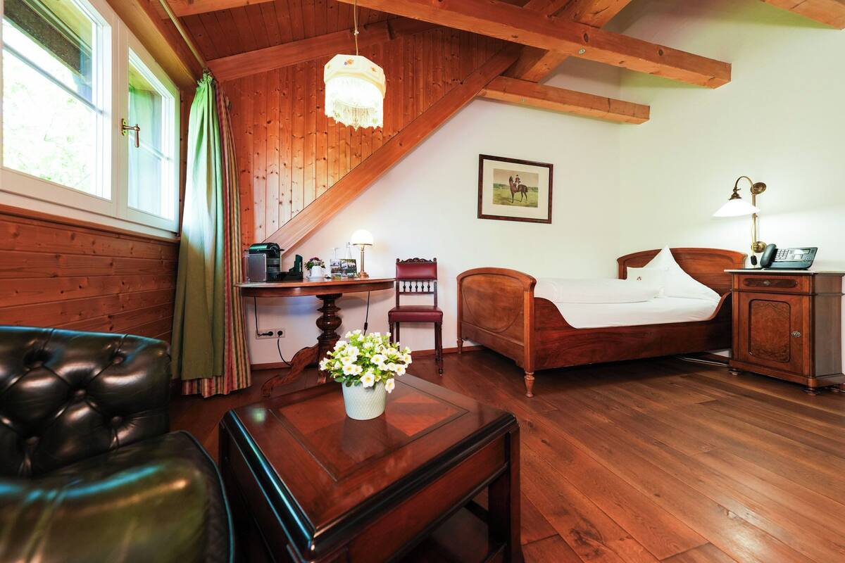 Una habitación acogedora con techo de madera, una cama, un escritorio con lámpara, una silla y un sofá de cuero.
