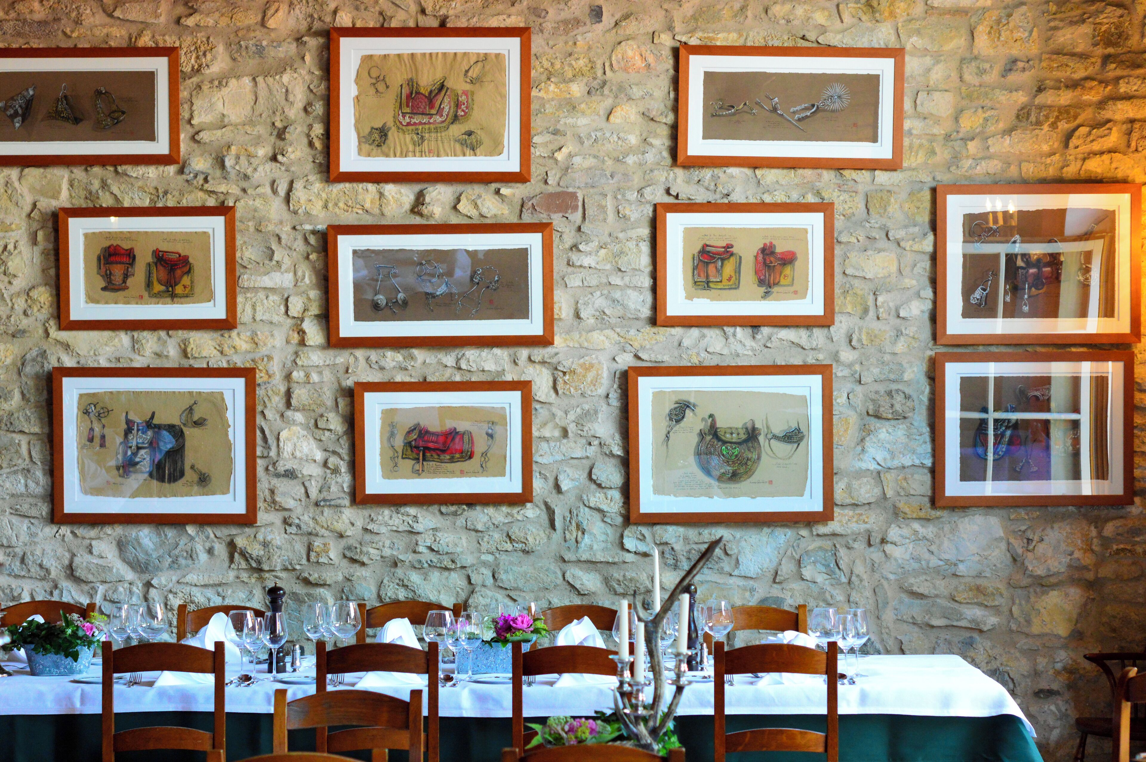 Ein Restaurant mit Steinwänden und gerahmten Kunstwerken. Tische sind mit weißen Tischdecken, Weingläsern und Holzsesseln gedeckt.
