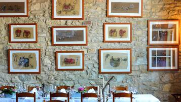 Ein Restaurant mit Steinwänden und gerahmten Kunstwerken. Tische sind mit weißen Tischdecken, Weingläsern und Holzsesseln gedeckt.
