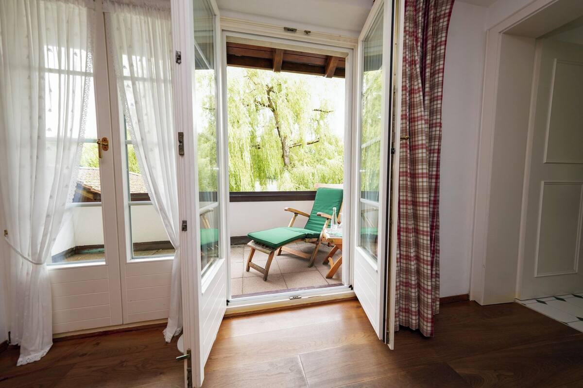 Una habitación con puerta de vidrio corrediza que da a un balcón con una silla verde y una mesa.