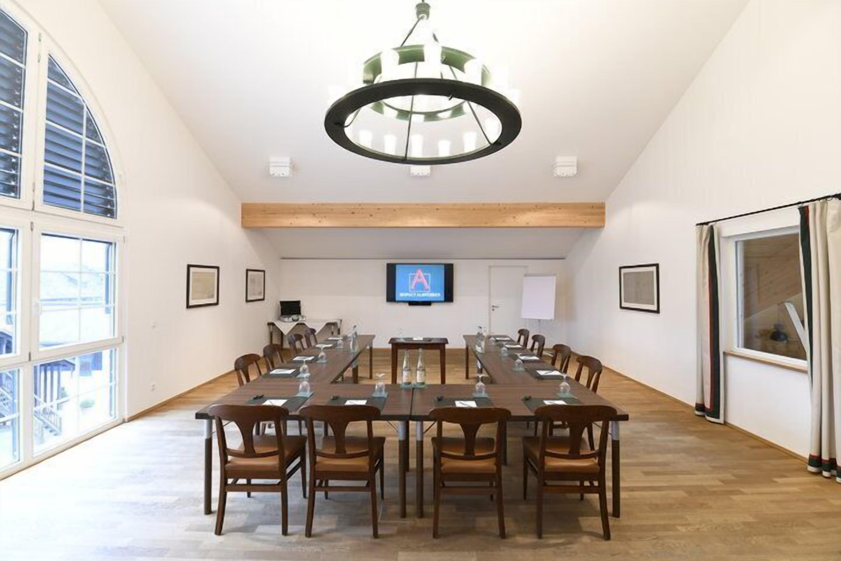 A conference room with a long table, chairs, a chandelier, a TV screen, and framed pictures on the walls.