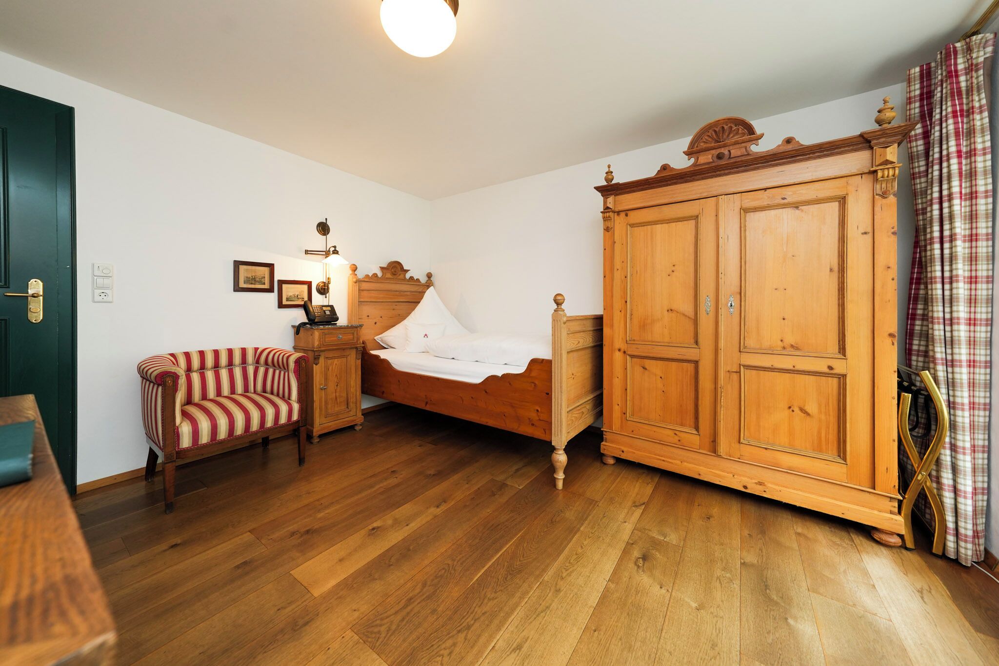 Ein Schlafzimmer mit einem hölzernen Bett, einem gestreiften Sessel, einem Holzschrank und einer grünen Tür.
