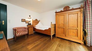 Ein Schlafzimmer mit einem hölzernen Bett, einem gestreiften Sessel, einem Holzschrank und einer grünen Tür.