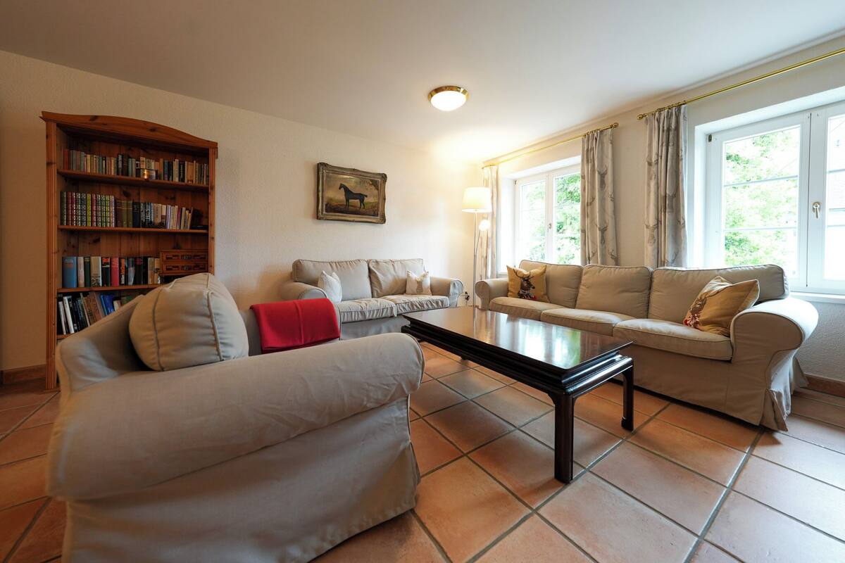 Una sala de estar con sofá, mesa de centro, estantería y ventana con cortinas.