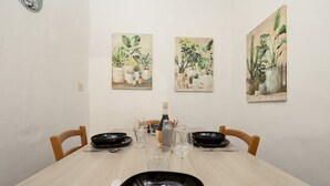 A dining table set with black plates, clear glasses, and a bottle of wine. There are three paintings of plants on the wall above the table. - Santo Spirito Urban Apartment (Florence)