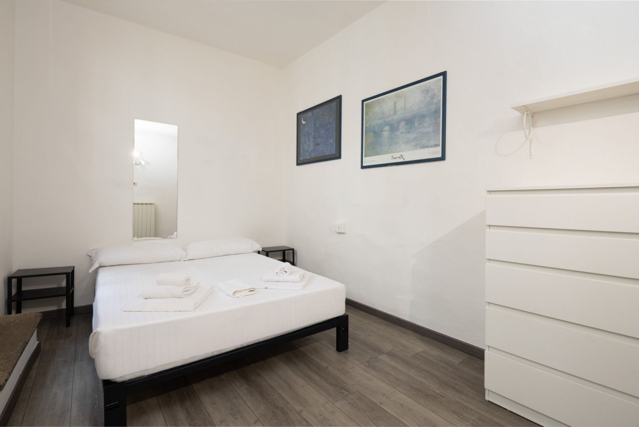 A bedroom with a bed, a bedside table, a dresser, and two framed pictures on the wall.