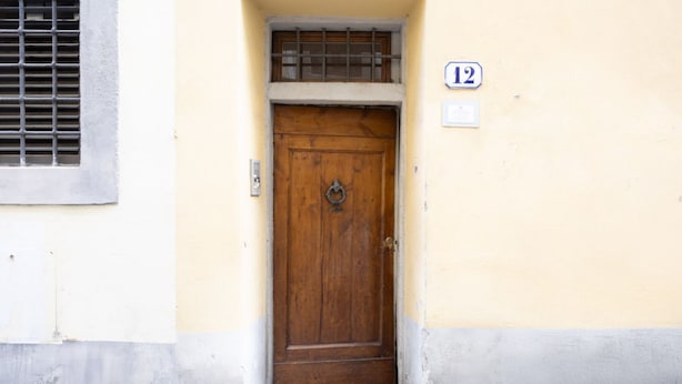 A wooden door with a metal latch, a window with a metal grill, and a number '12' sign on the wall. - Santo Spirito Urban Apartment (Florence)