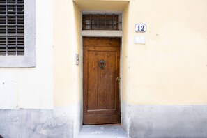 A wooden door with a metal latch, a window with a metal grill, and a number '12' sign on the wall.
