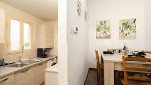 A compact kitchen with a sink, stove, and a dining area with a table set for two. - Santo Spirito Urban Apartment (Florence)