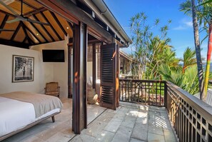 A bedroom with a bed, a chair, a television, and a view of a garden with palm trees.
