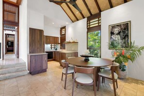 A modern kitchen with wooden cabinets, a dining area with a round table and chairs, and a large potted plant.