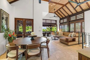 A spacious living area with a round dining table, seating, a sofa, and a balcony with outdoor furniture.