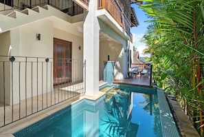 A poolside area with a clear view of a swimming pool, a wooden door, and a balcony with a railing.