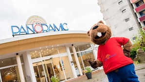 A mascot in front of a building with a sign reading "PANORAMIC."