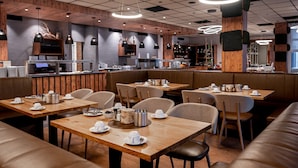 A modern restaurant with wooden tables and booths, a bar area, and pendant lighting.