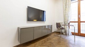 Un soggiorno moderno con una televisione a schermo piatto montata a parete, un mobile contenitore grigio, un pavimento in legno a spina di pesce, un tavolo da pranzo con una sedia e un'ampia finestra con tende.