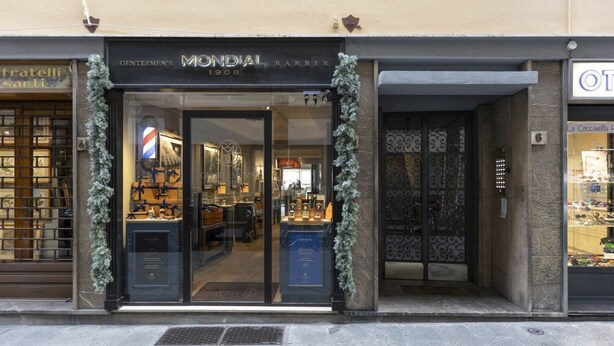 Una vetrina con un cartello che riporta "MONDIAL BARBER" e l'esposizione di strumenti da barbiere all'interno.