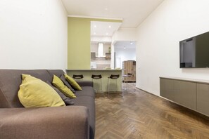 Una sala de estar moderna con un sofá, televisión y una cocina al fondo.