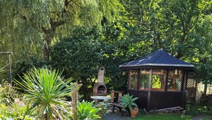 A garden with a gazebo, a barbecue grill, and a lounge chair. - Cozy newly built vacation apartment in quiet wooded surroundings (Dippoldiswalde)