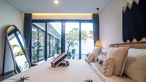 A modern hotel room with a large bed, a mirror, and a view of the outdoors through large windows. - Villa CanSavina - 3 Rooms - Center Of Seminyak (Bali)