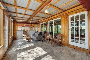 A spacious indoor area with a wooden ceiling, a sofa, chairs, and a dining table.