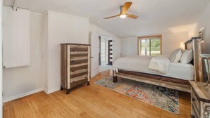 A bedroom with a bed, a ceiling fan, a wooden dresser, and a door leading to another room. - Lakefront Retreat: Private Dock | King Bedrooms (Burnet County)