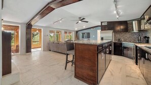 A spacious kitchen with a large island, dark cabinetry, and a view to the outdoors. - Lakefront Retreat: Private Dock | King Bedrooms (Burnet County)